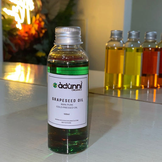 A bottle of Adunni Organics Grapeseed Oil with a label showing the product name and the fact that it is a cologne for men. The bottle is set against a backdrop of various colored oils.
